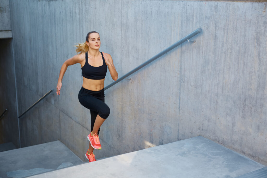 Mujer activa subiendo escaleras al aire libre, cuidando su rutina deportiva